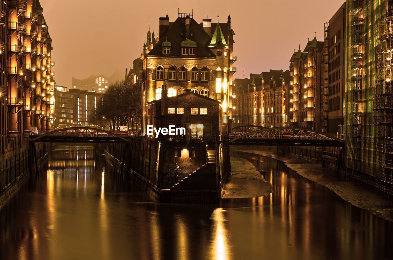 Bridge over river amidst buildings in city at night