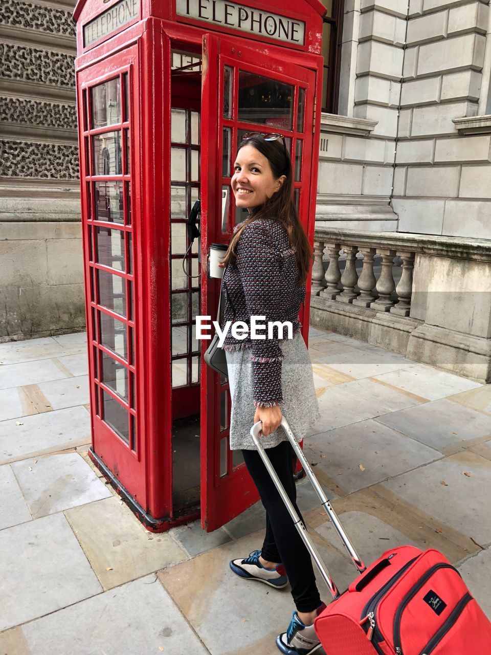 Portrait of smiling young woman entering telephone booth