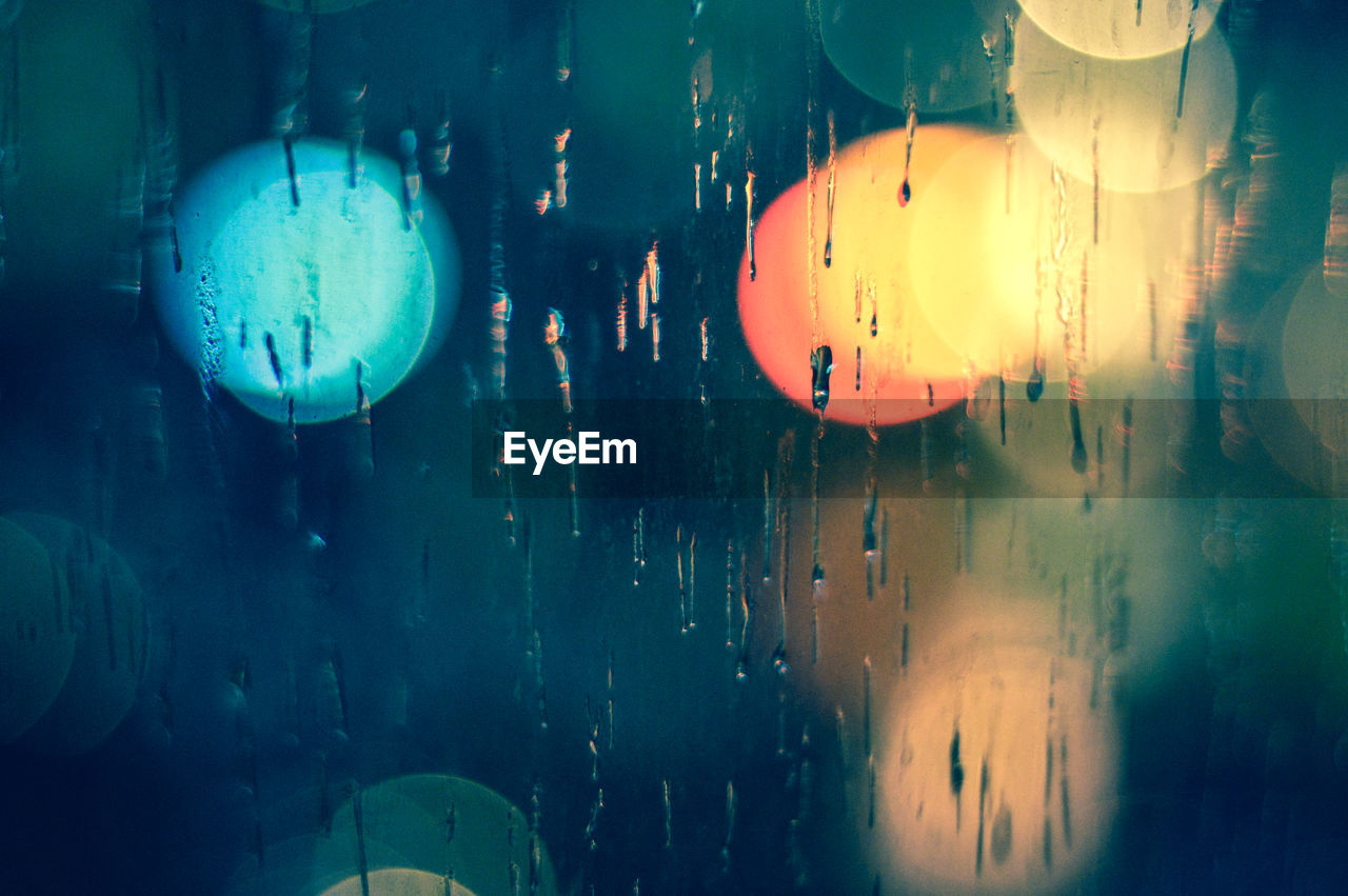 Defocused image of illuminated lights seen through window during monsoon