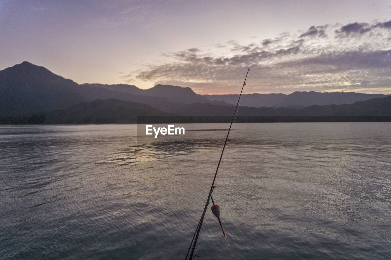 Fishing rod against river and sky at dusk