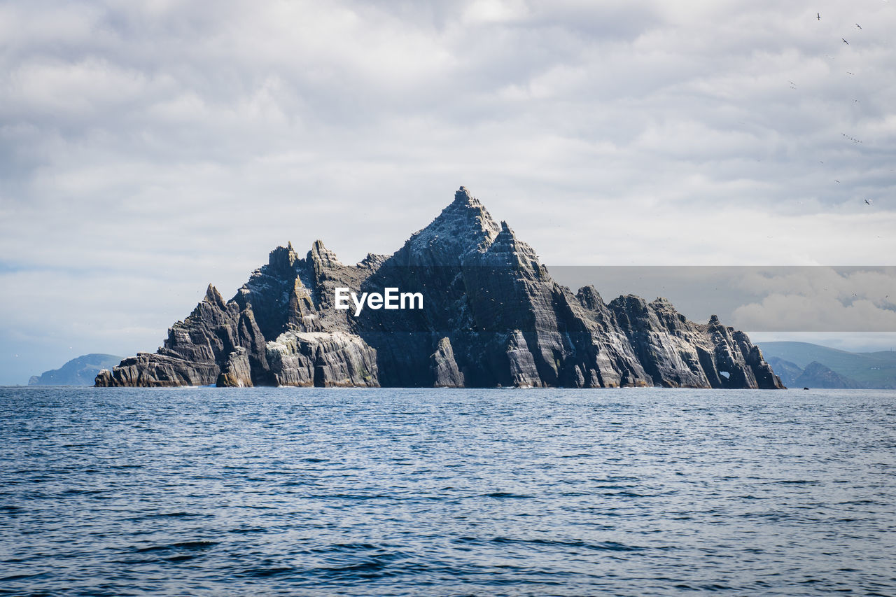 Scenic view of sea by mountain against sky