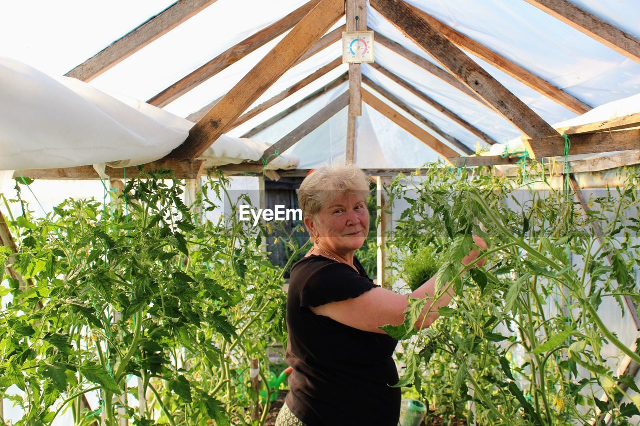 Side view of portrait woman standing by plants in greenhouse