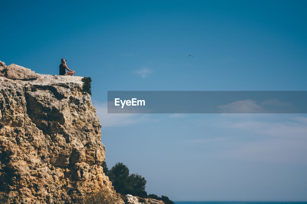 Low angle view of woman sitting on cliff by sea