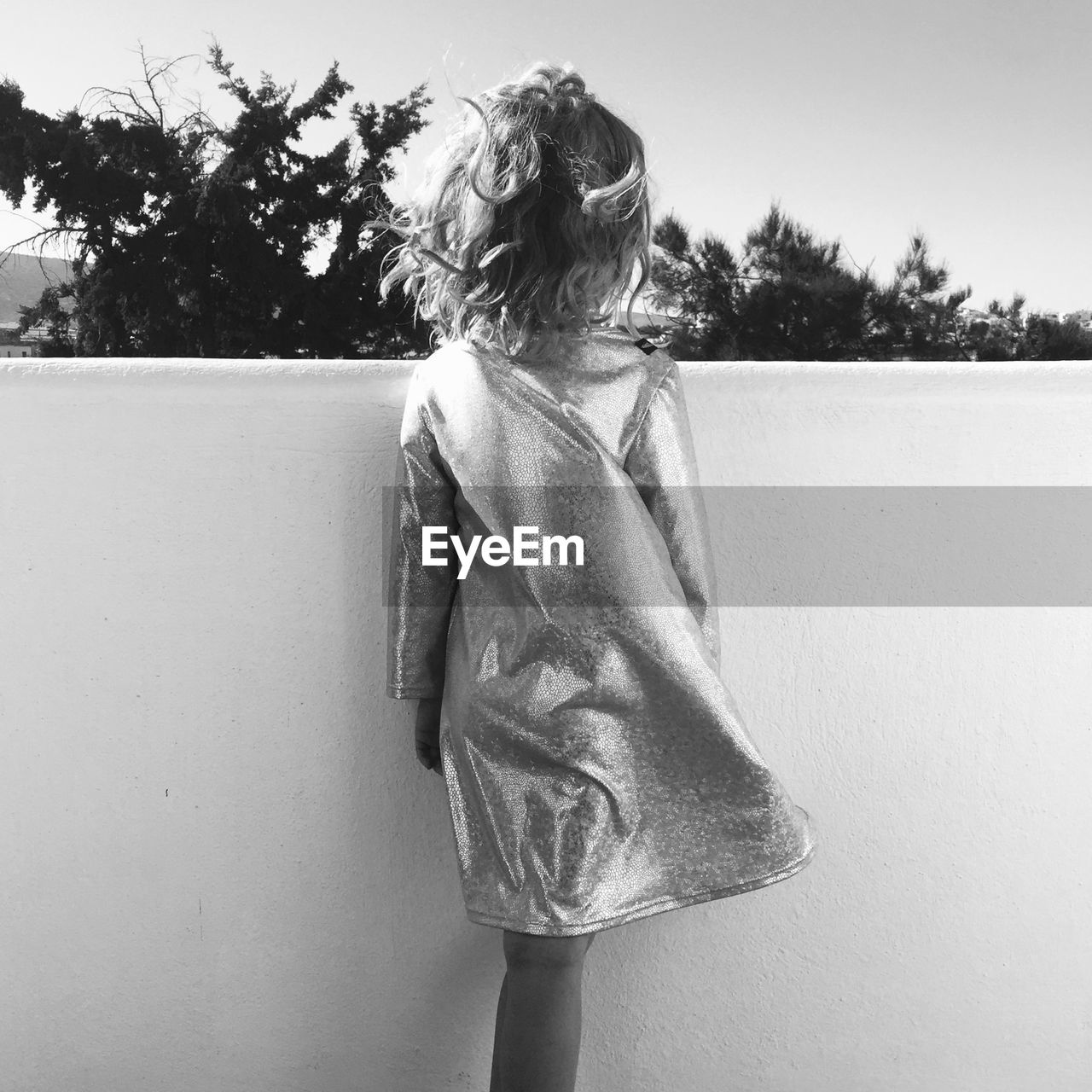 Girl standing by wall and trees against sky