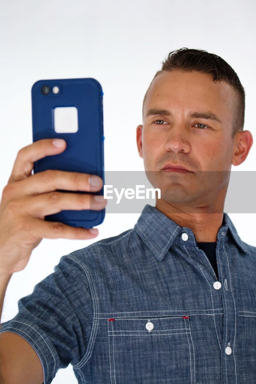 Confident man taking selfie with smart phone against white background