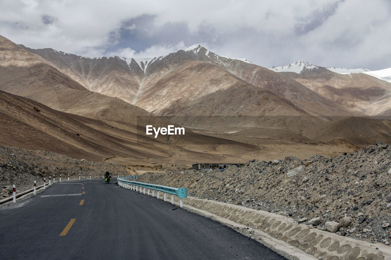 A flat newly built asphalt road calls the foot of the snowy mountain ahead
