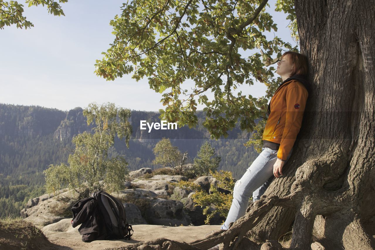 Woman leaning on tree against mountain