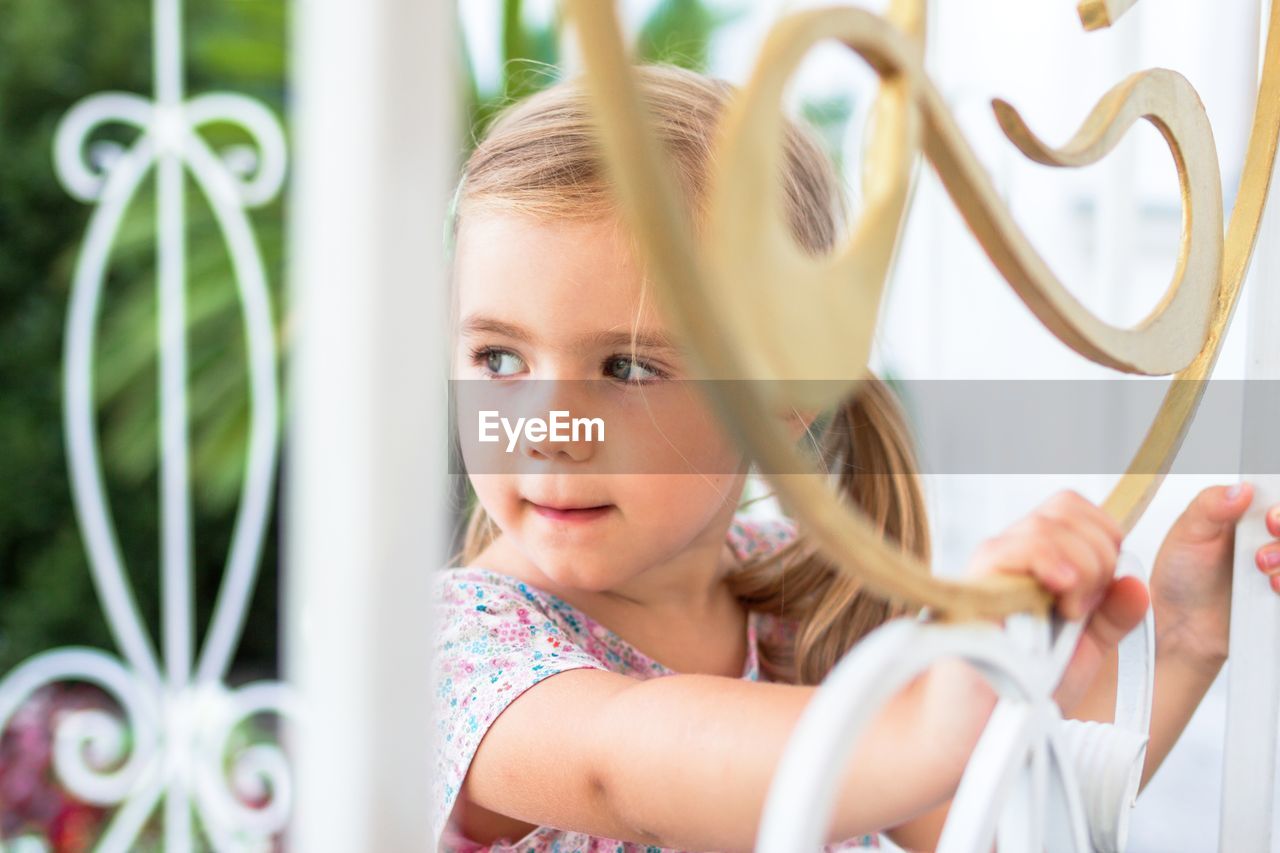 Young girl with blonde hair smiling behind a charming white picket fence