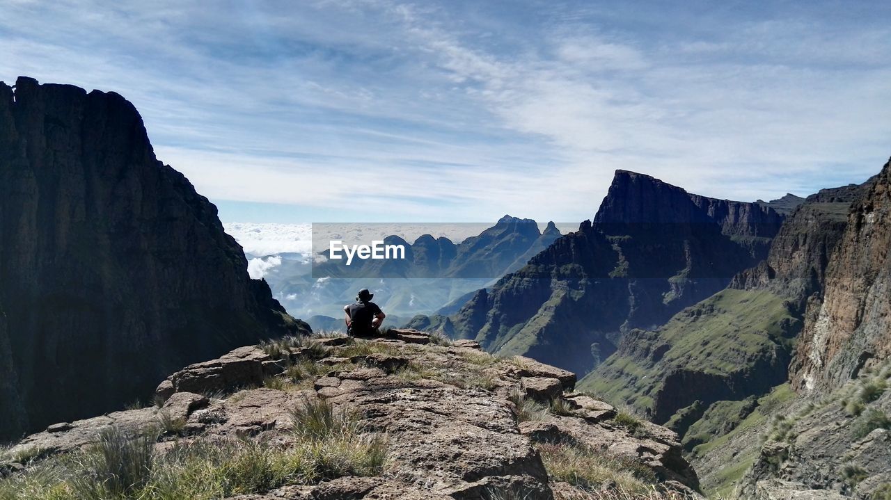 Rear view of man sitting on cliff against sky