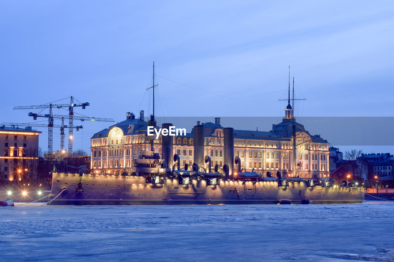 River by illuminated city against sky at dusk