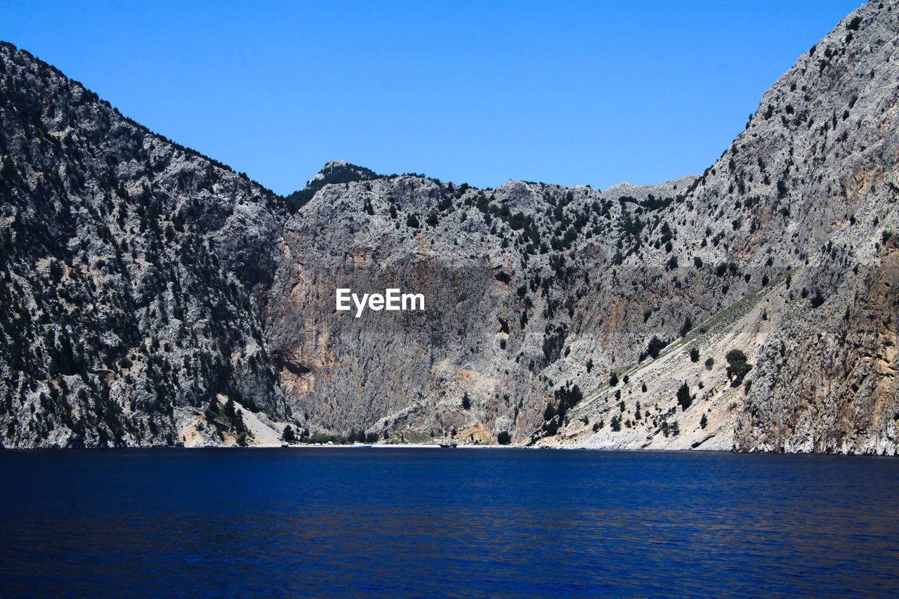 Scenic view of sea and mountains against clear blue sky