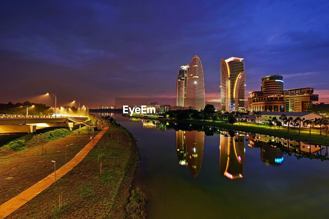 Illuminated buildings reflecting in river against sky at night