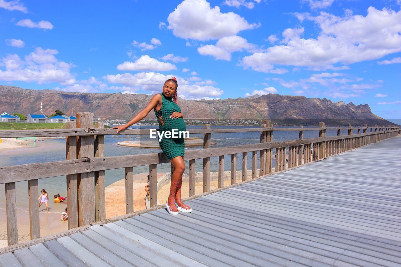 Happy black pregnant woman standing on a wooden bridge the beach