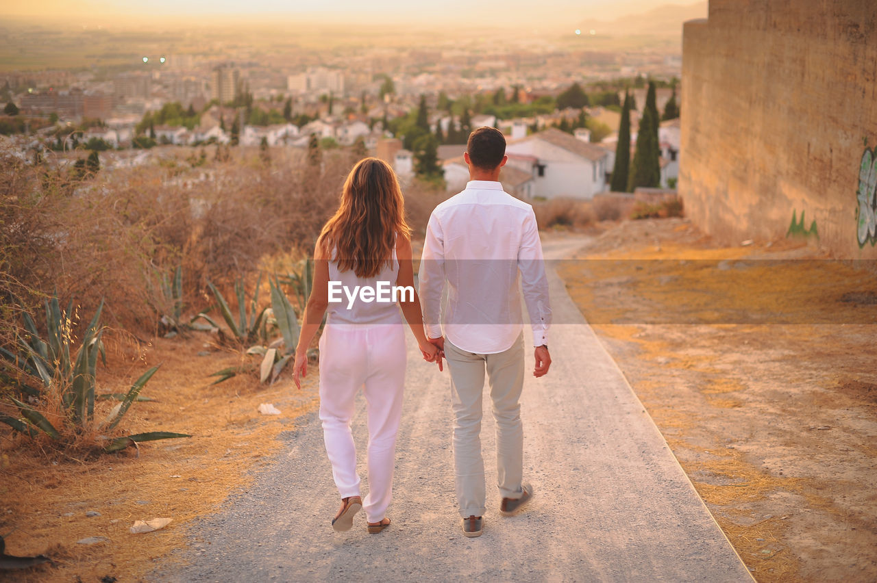 Rear view of couple walking on road during sunset