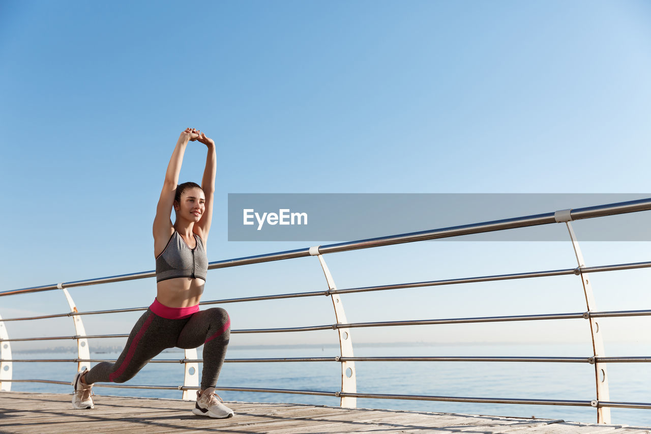 Full length of woman exercising by railing while standing against sea