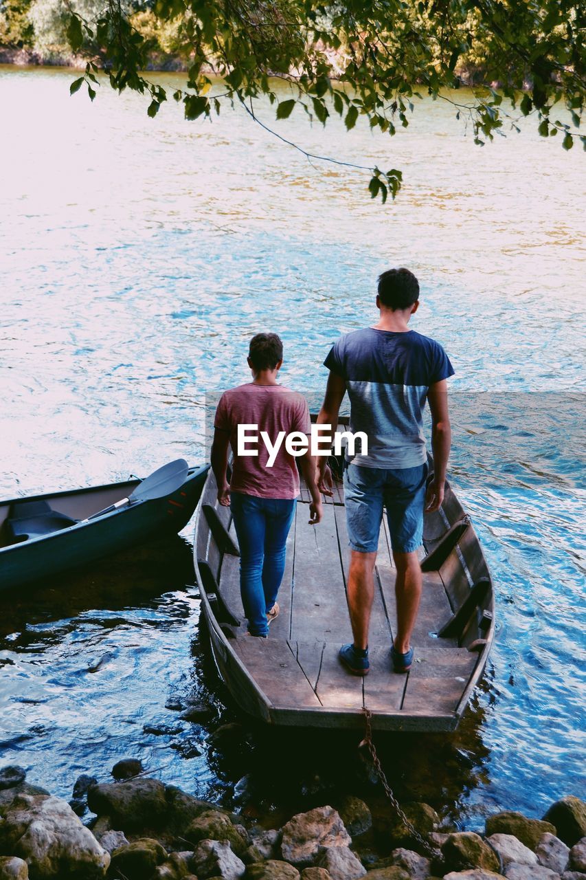 Rear view of men standing on boat sailing in river