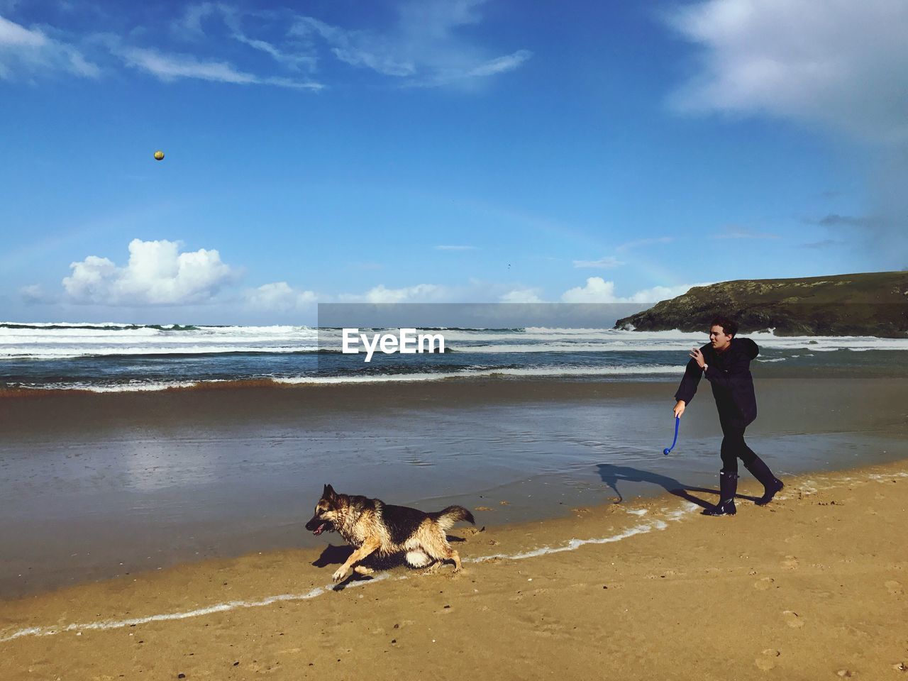 Man with dog running at beach against sky