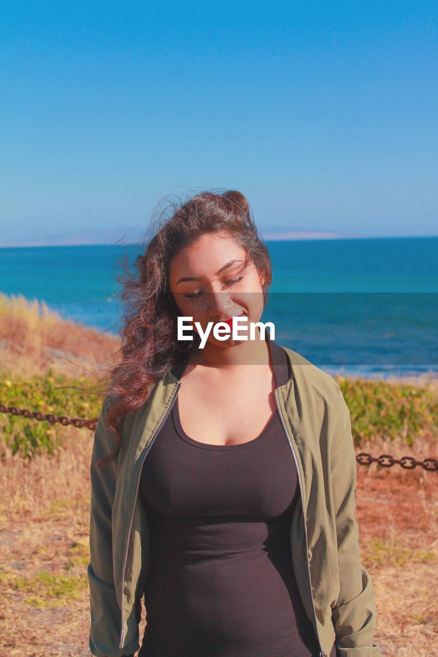 Young woman standing against sea on sunny day