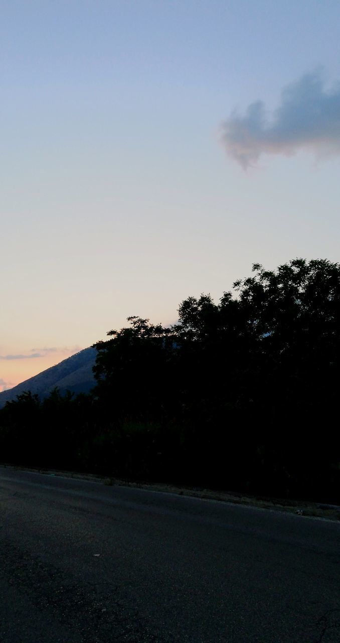 Silhouette trees by road against sky at sunset