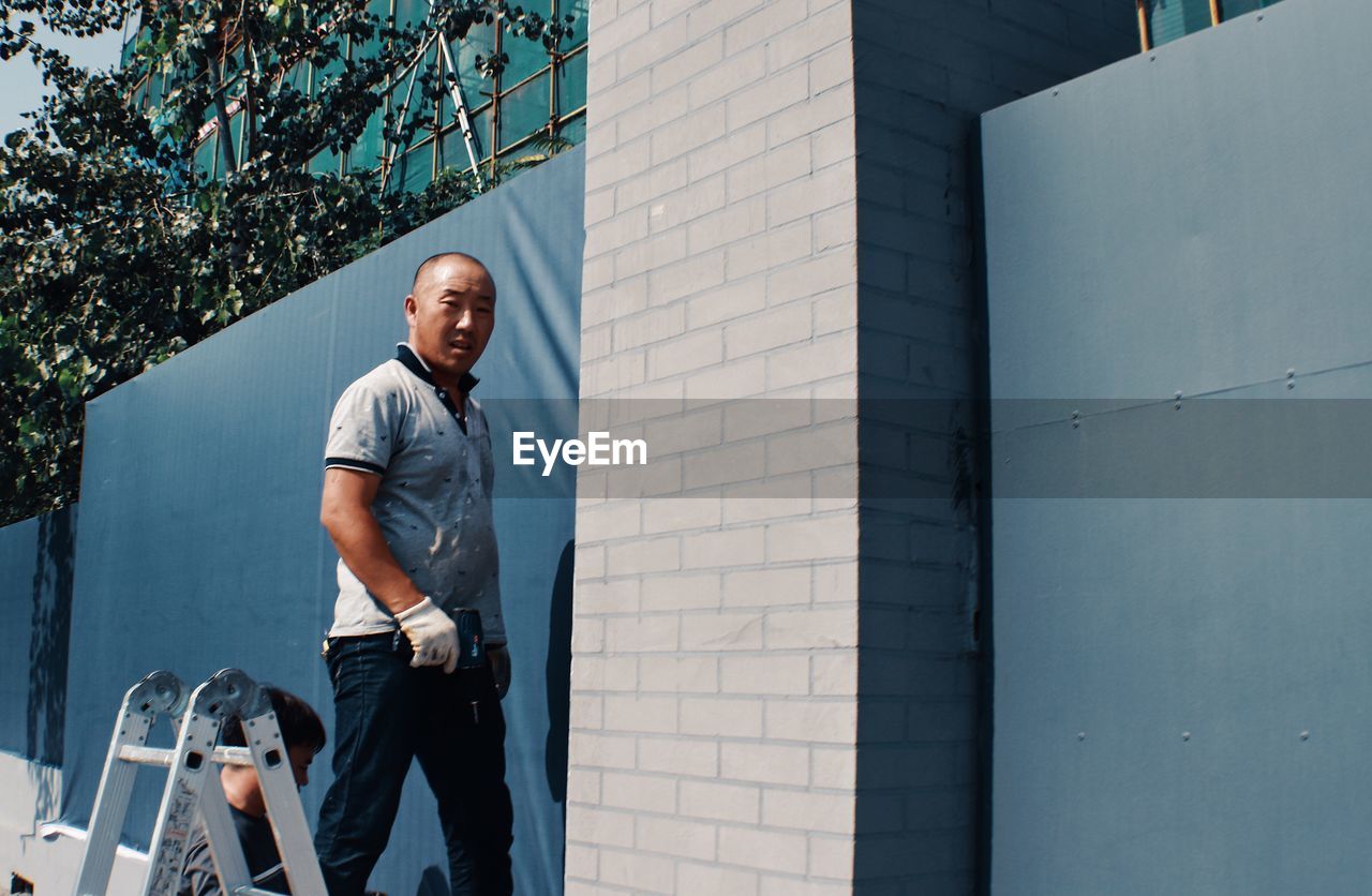 FULL LENGTH PORTRAIT OF SMILING MAN STANDING AGAINST WALL