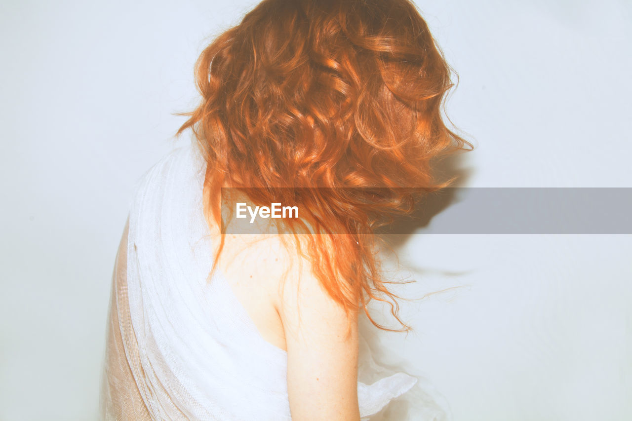 Rear view of woman with redhead wrapped in fabric against white background