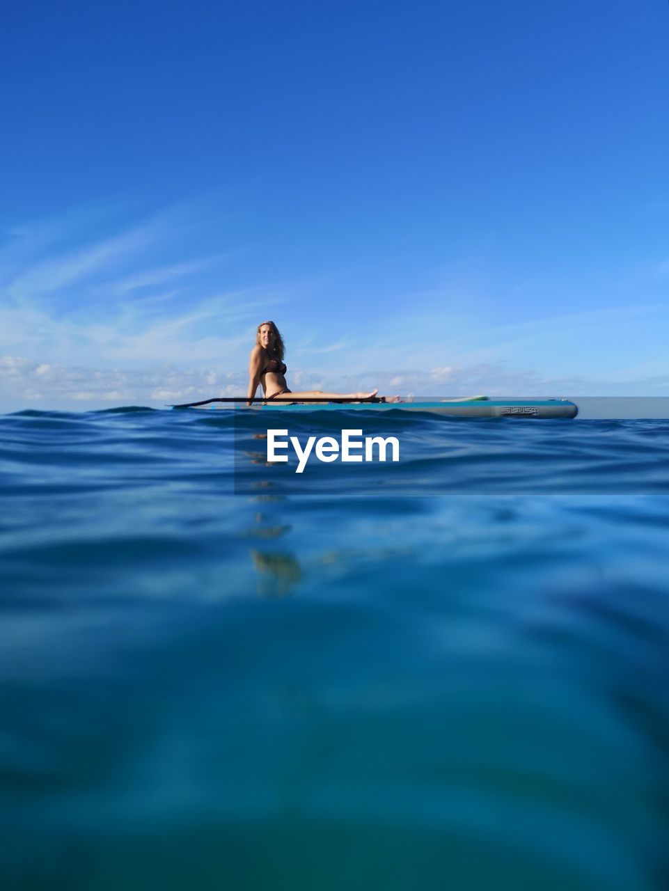 Surface level of woman sitting on paddle board in sea against sky