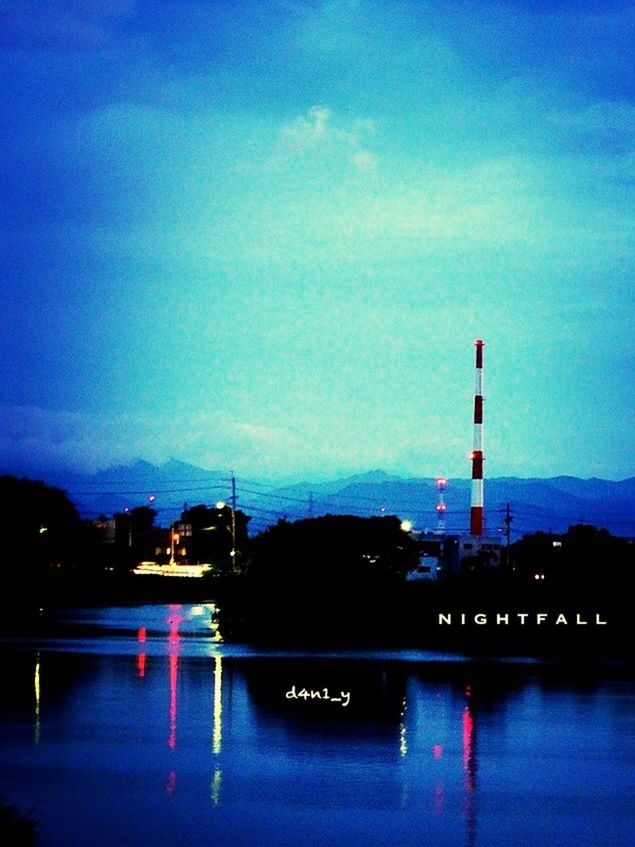 RIVER BY ILLUMINATED FACTORY AGAINST SKY