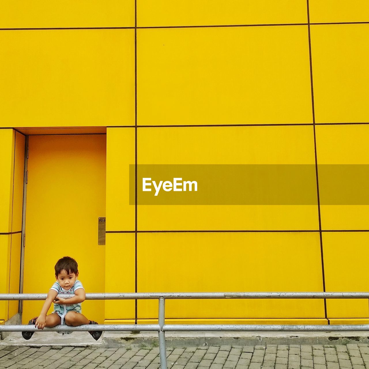 Boy hanging on railing against yellow building