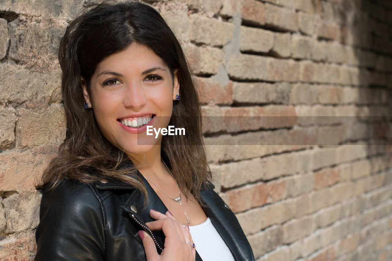 Portrait of smiling young woman standing against brick wall