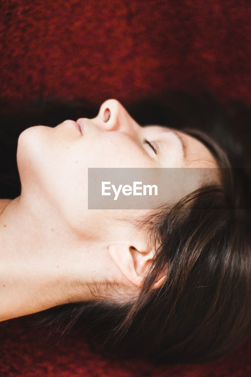 CLOSE-UP PORTRAIT OF WOMAN LYING DOWN ON RED