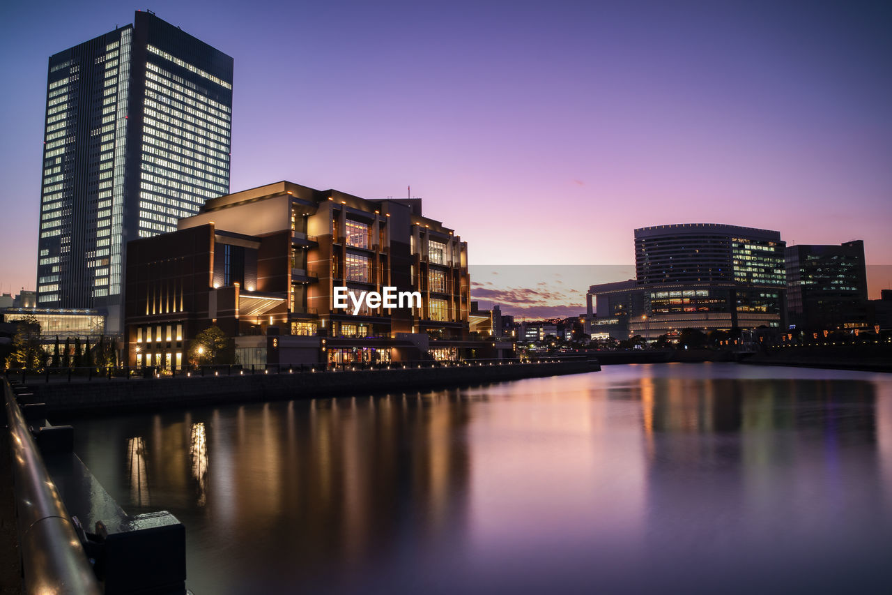 Illuminated buildings by river against sky at night