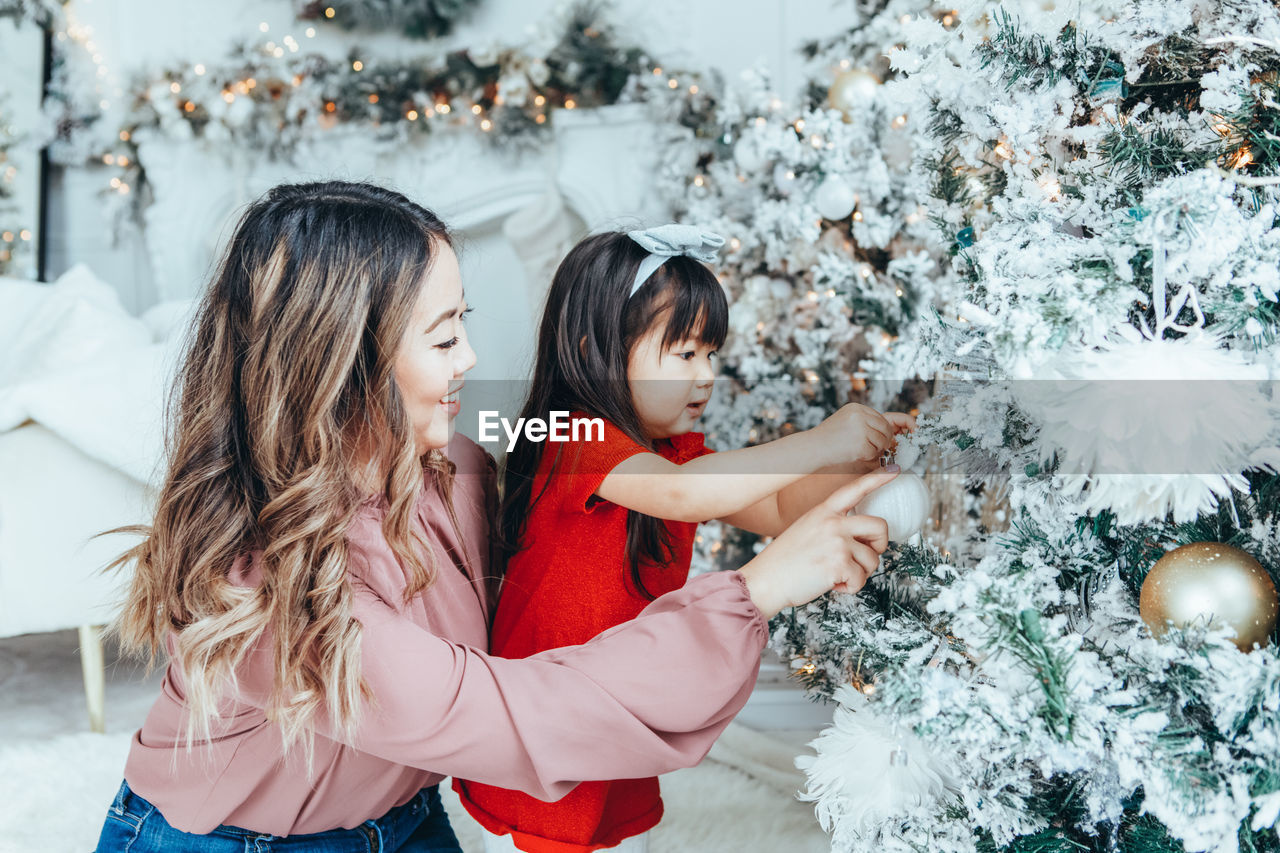 Happy mother and daughter touching christmas tree at home