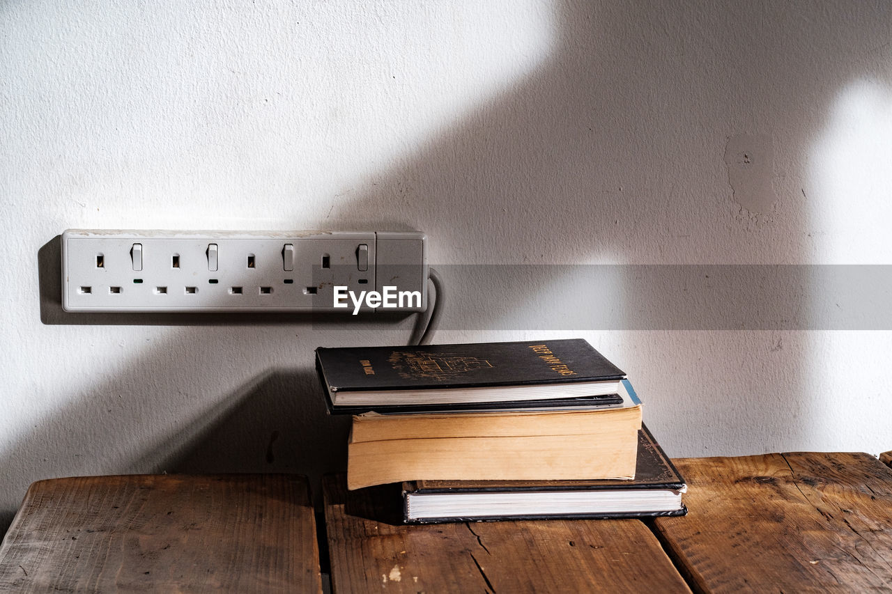 STACK OF BOOKS ON TABLE BY WALL