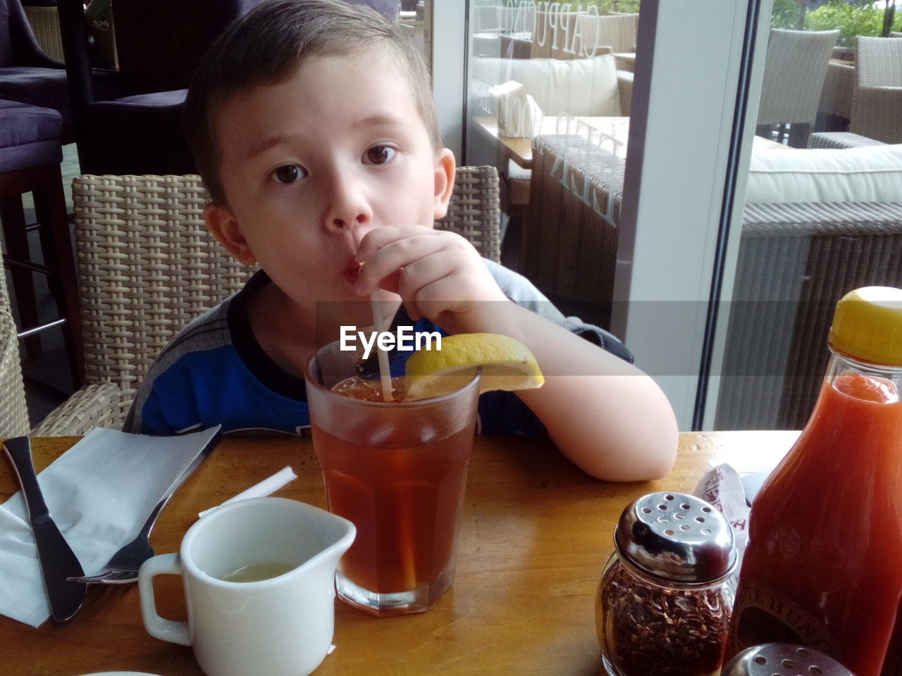 Portrait of boy having drink at table in restaurant