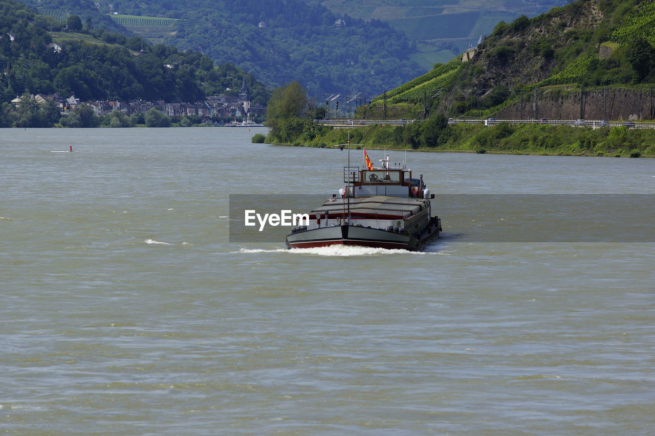 BOAT SAILING IN SEA AGAINST MOUNTAINS