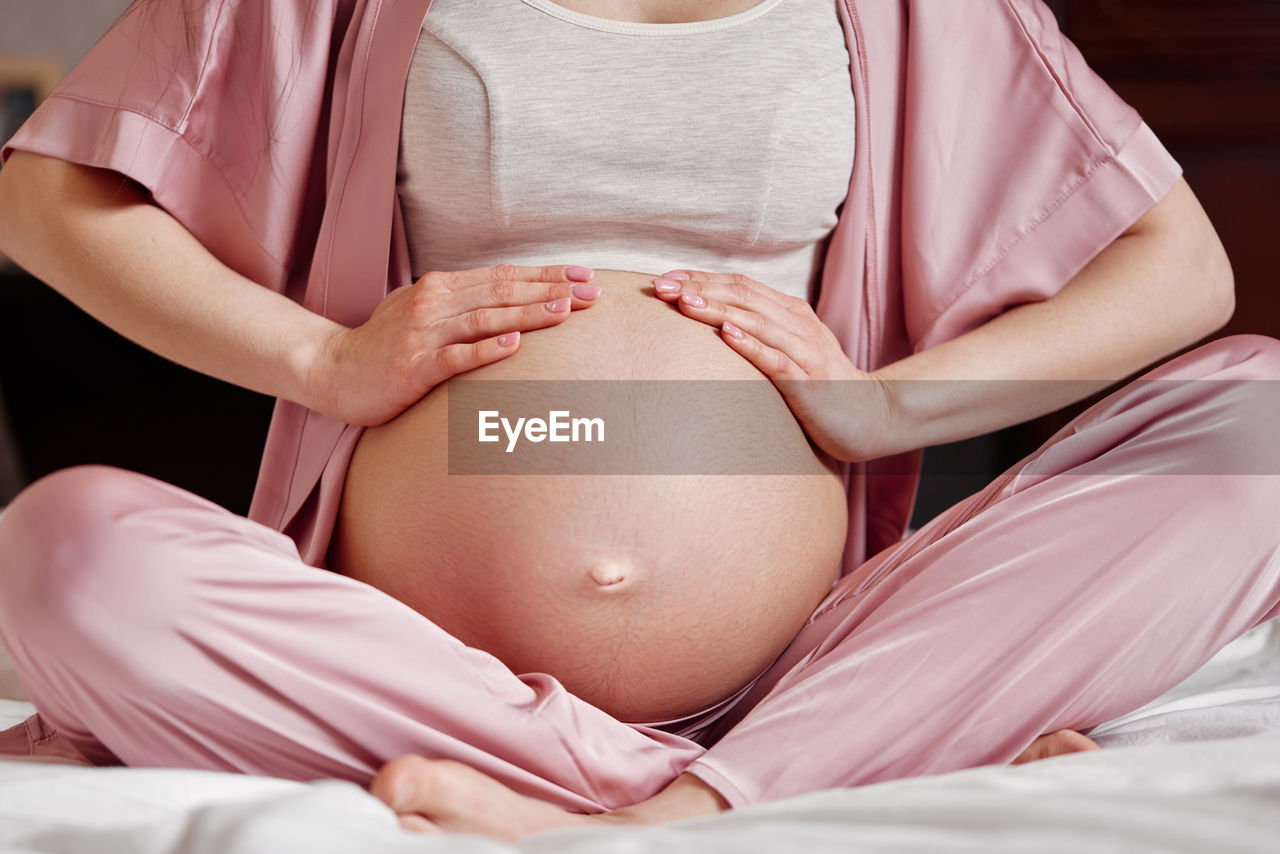 Midsection of pregnant woman touching belly sitting on bed