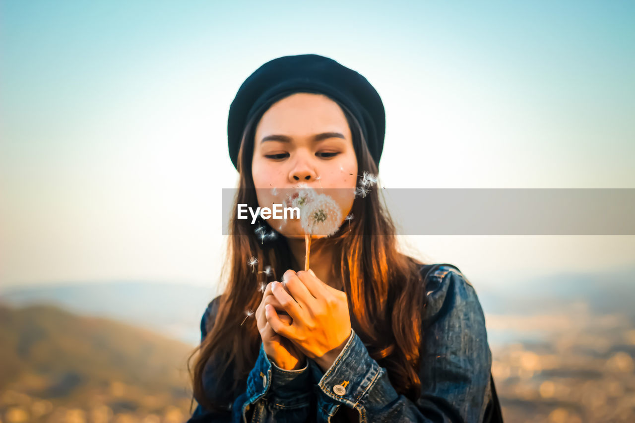 Portrait of young woman holding camera against sky during sunset