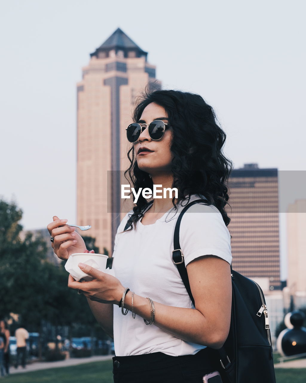 Woman having food while standing against buildings in city