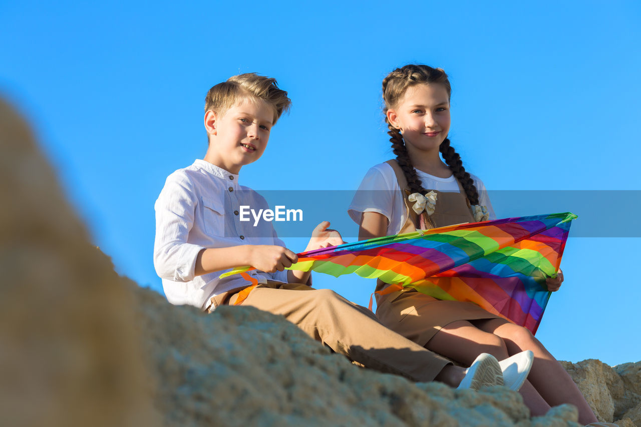 Teenage children are sitting on a high mountain thinking how to assemble a kite.