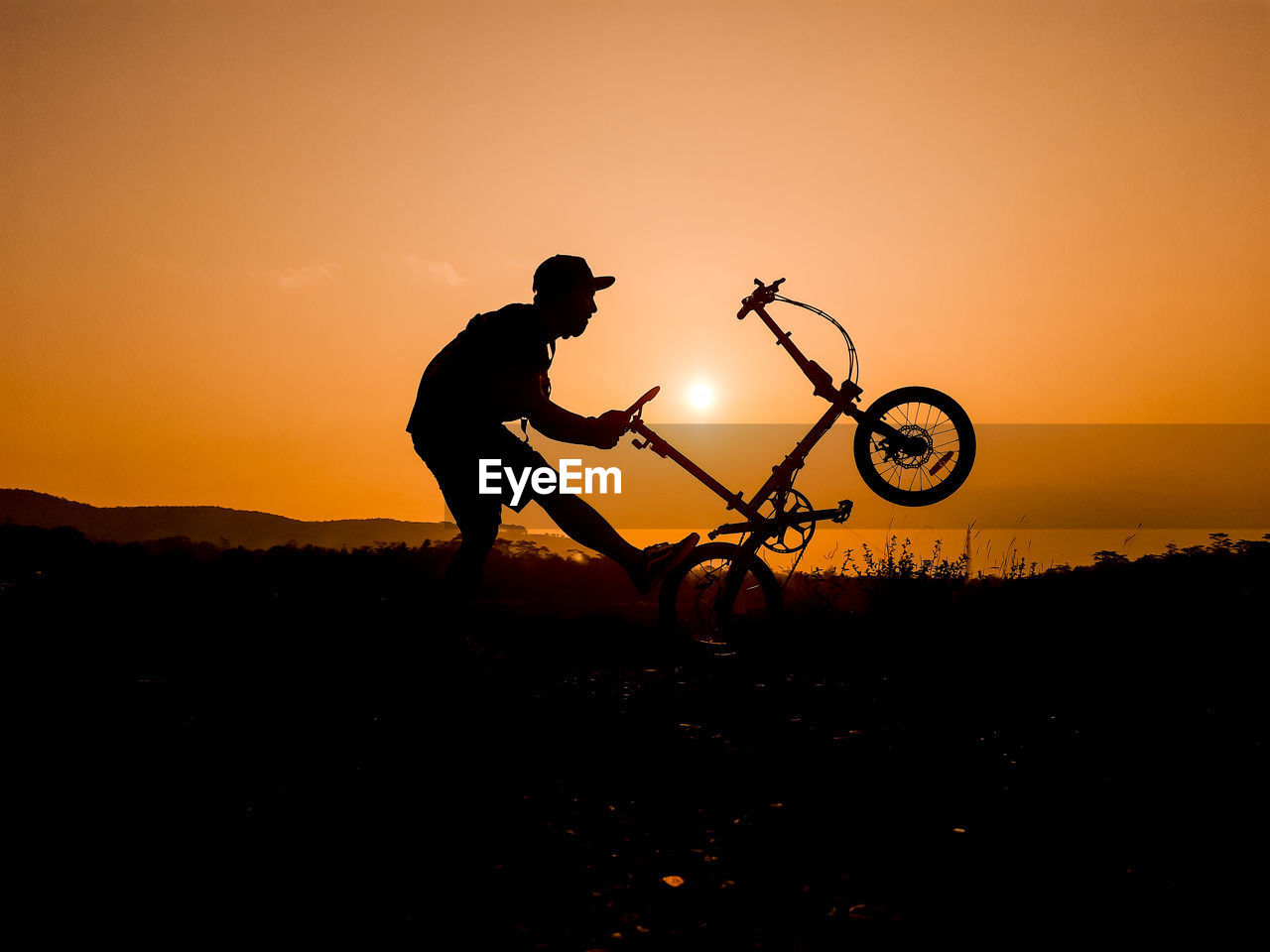 Silhouette man riding bicycle on land against sky during sunset