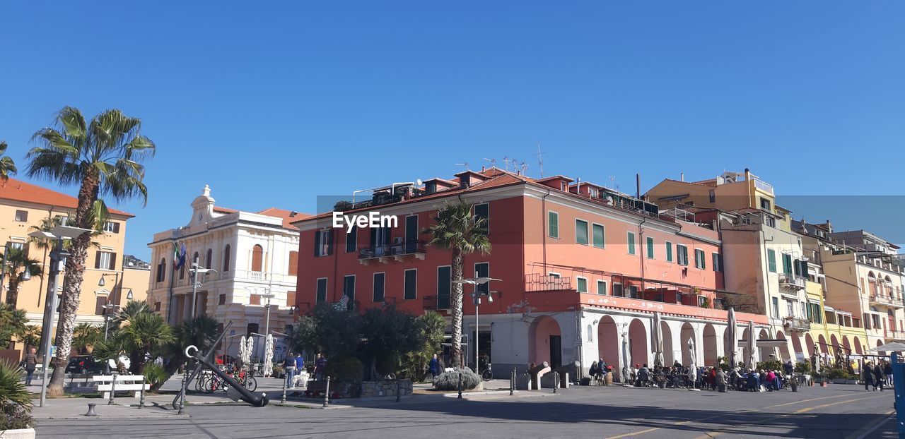 architecture, town, building exterior, neighbourhood, city, built structure, street, town square, sky, clear sky, downtown, nature, sunny, building, travel destinations, blue, road, cityscape, plaza, residential area, city street, transportation, tree, travel, vacation, residential district, sunlight, tourism, day, plant, tropical climate, palm tree, city life, outdoors, the past, history, urban area, house, mode of transportation, car, copy space, motor vehicle