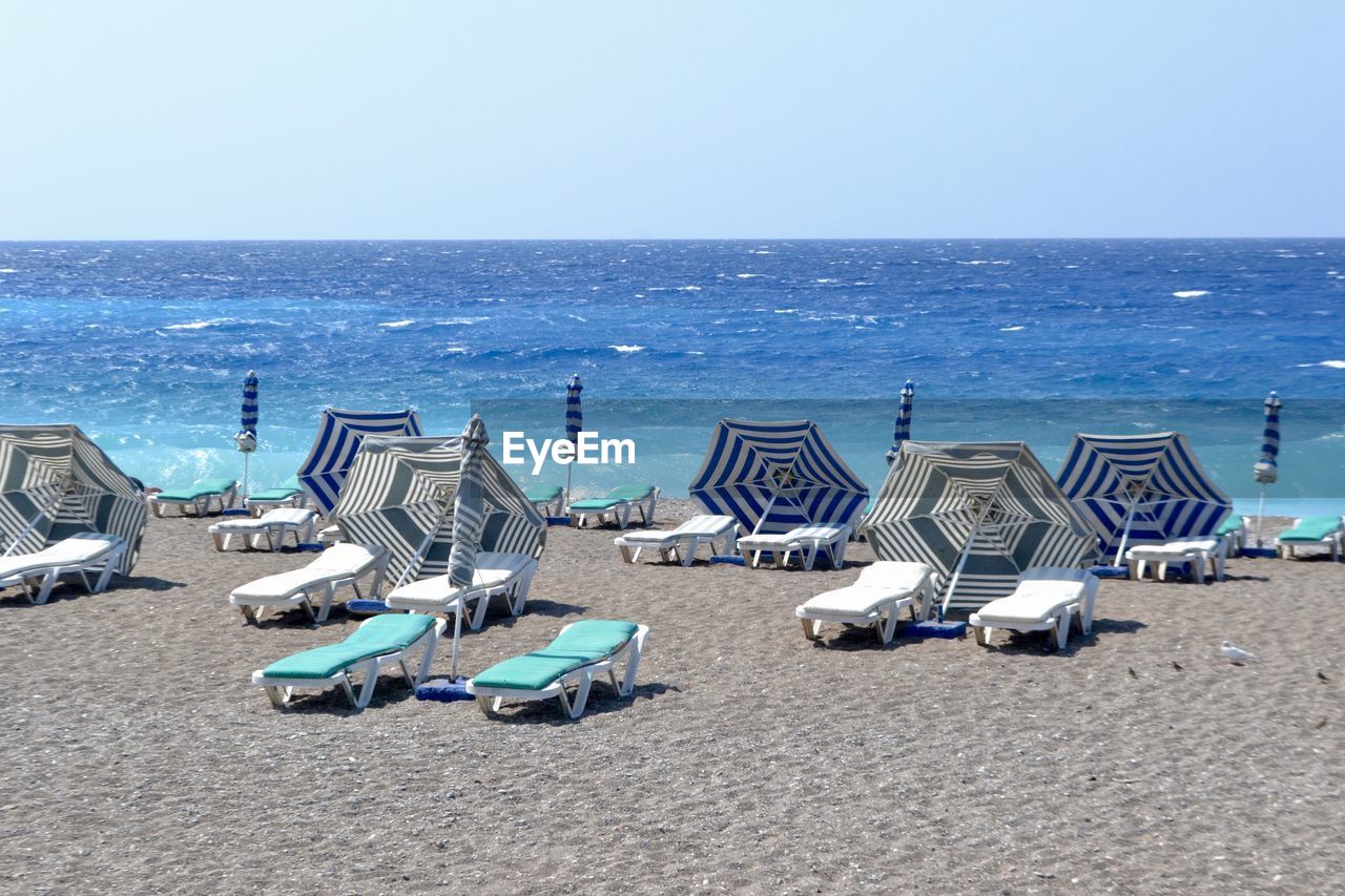 Lounge chair and beach umbrellas on beach against clear sky