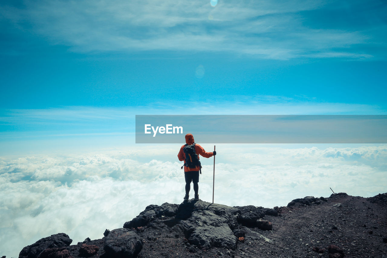 Rear view of man standing on cliff against cloudy sky