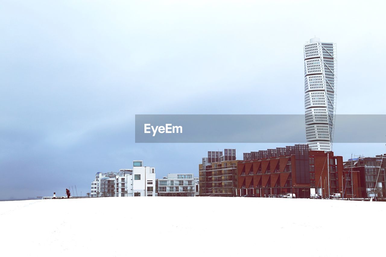 Snow covered field by cityscape against sky