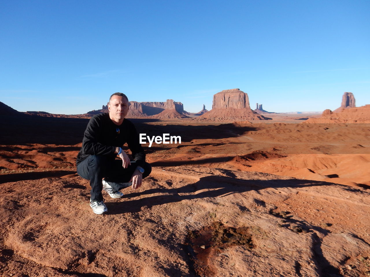 YOUNG MAN SITTING ON ROCK AGAINST CLEAR SKY