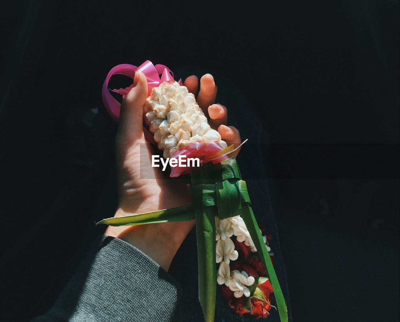 Cropped hand holding flower garland against black background