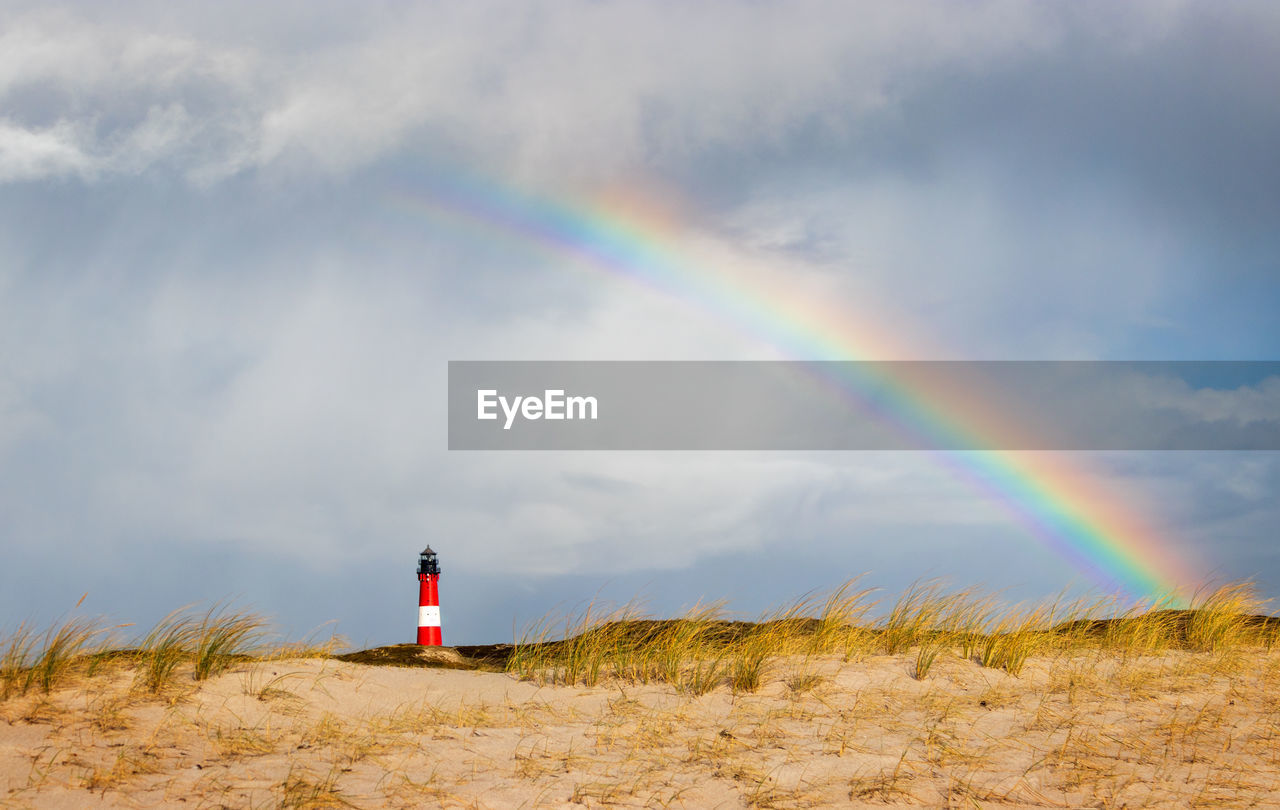 Lighthouse under rainbow at hörnum, sylt - rainy weather at dune landscape with special light