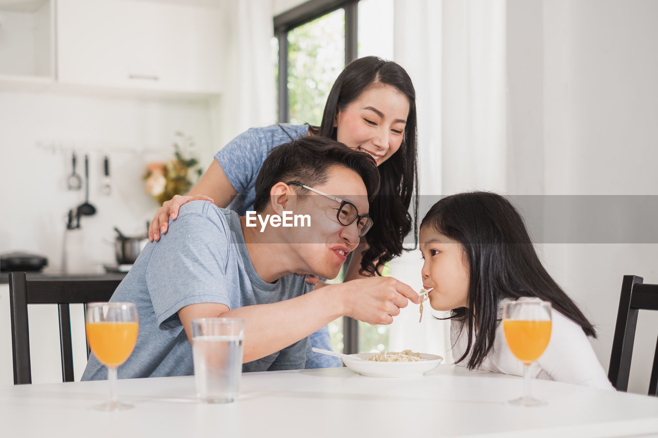 Father feeding food to girl while sitting at table