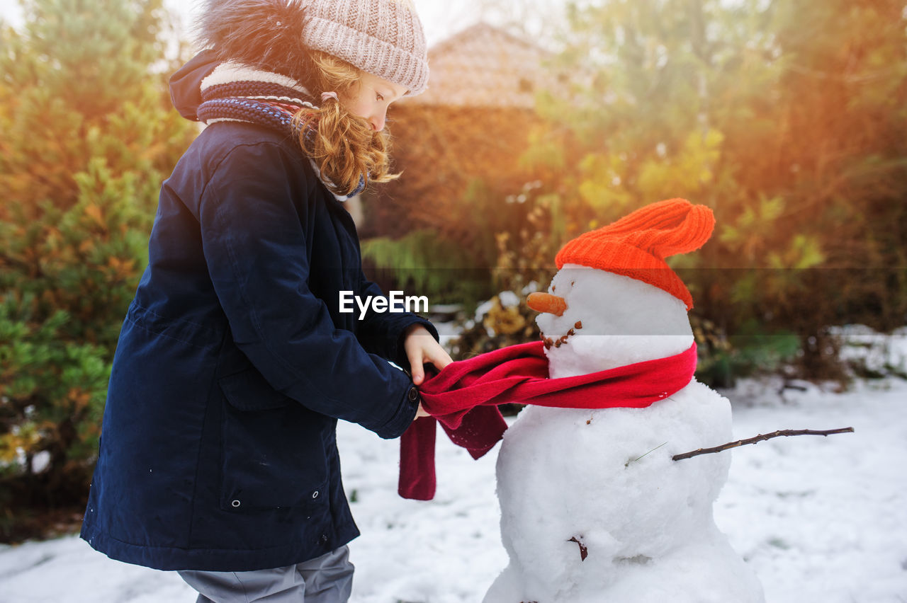 Side view of girl making snowman during winter