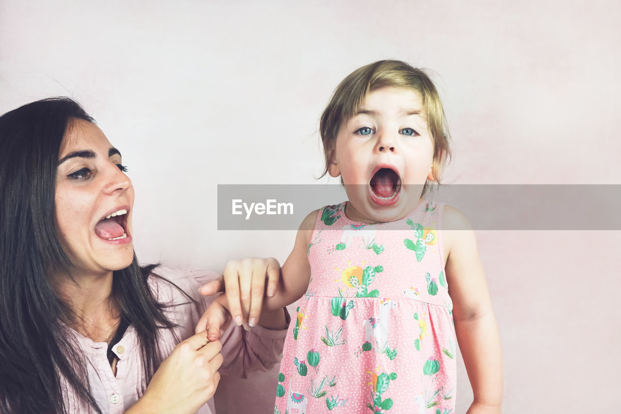 Mother carrying cute daughter standing against wall